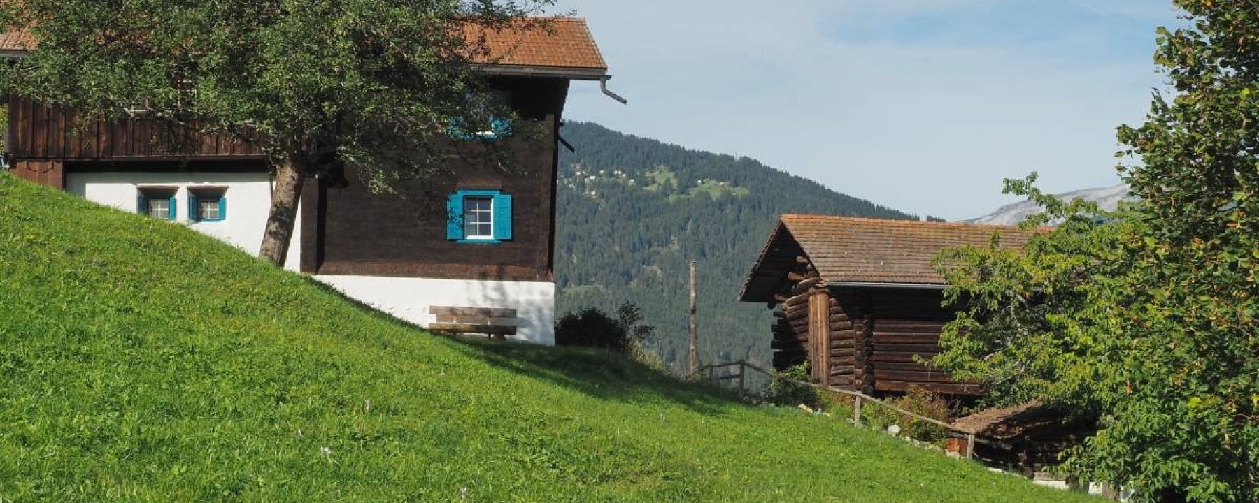 Vorbei an den sonnengebräunten Holzhäuser von Praden
