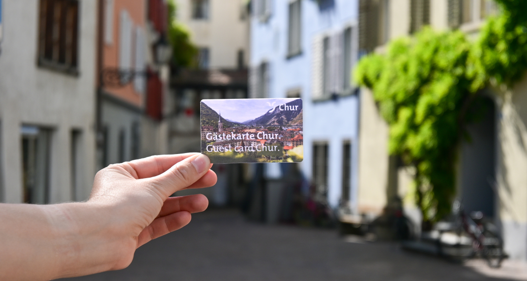 Guestcard Chur The city walls can be seen in the background, in the foreground a person is holding the guest card of Chur in his hands.