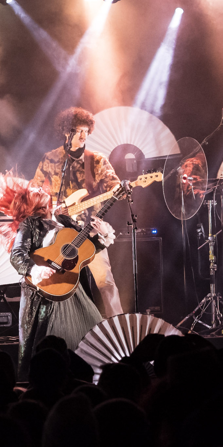 Arcas Rock (© Arcas Rock) Eine Band aus 4 Personen tritt auf der Bühne auf. Helle Scheinwerfer strahlen von oben, und weiße Fächer schmücken den Hintergrund.