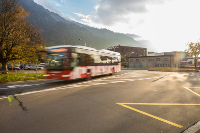 A red and white bus speeds by on a quiet road with mountains and a building in the background