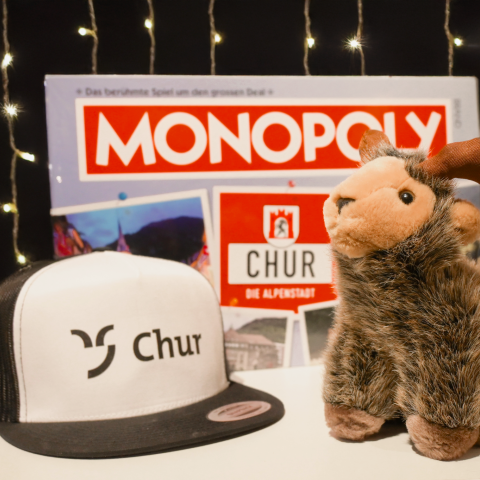 Monopoly, Mütze mit Chur Logo und ein Steinbock als Plüschtier vor einem leuchtenden Hintergrund