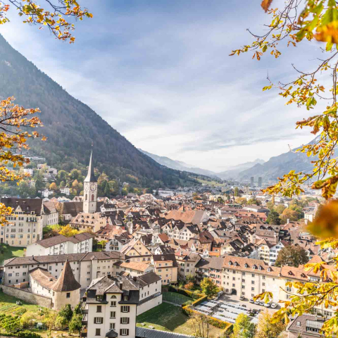 stadtansicht-herbst (© Mattias Nutt) Blick über die Altstadt von Chur im herbstlichen Kleid. Zwischen den bunten Blättern eingerahmt, ragen die Dächer der historischen Häuser und der markante Kirchturm hervor, während im Hintergrund die Berge das Stadtbild umrahmen.