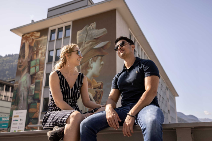 Mann und Frau sitzend vor einem Gebäude mit Street Art Fassade