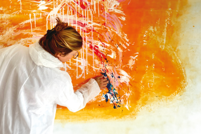 A person in a white coat paints an abstract mural with bold orange and white strokes