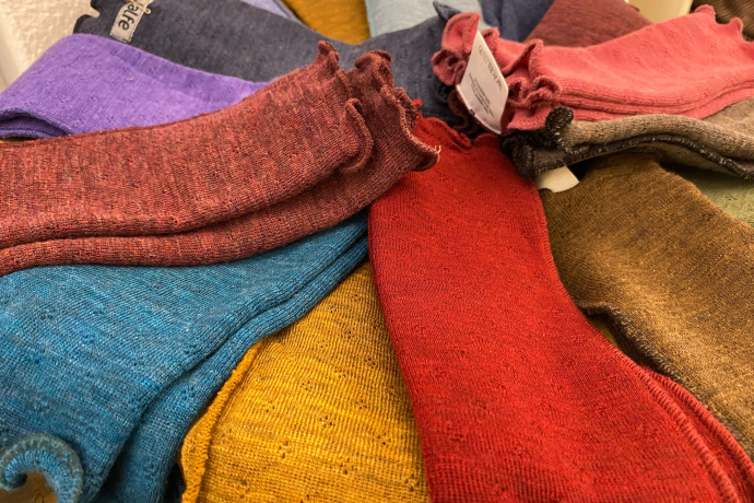 Ein Stapel farbenfroher Wollsocken in verschiedenen Tönen wie Rot, Blau, Gelb, Lila und Braun liegt ausgebreitet auf einem Tisch.
