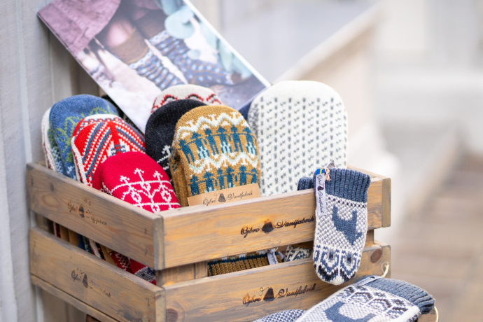 Holzkiste mit handgestrickten Fäustlingen und Socken in verschiedenen Farben und Mustern, ausgestellt auf einem kleinen runden Tisch vor einem Gebäude