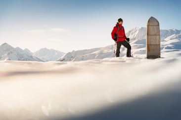 Schneeschuhwanderer macht eine Pause beim Obelisken auf dem Dreibündenstein