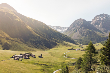 Ein Tal mit einem kleinen Dorf, umgeben von majestätischen Bergen und üppiger Natur.