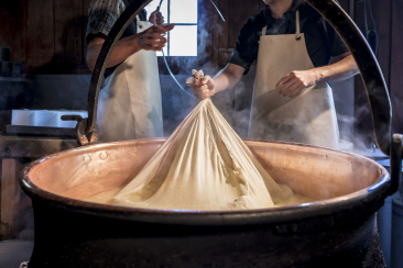 Zwei Personen stehen um einen grossen Topf und produzieren Käse