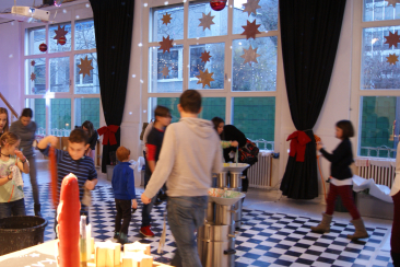 Kinder und Erwachsene ziehen Kerzen im Jugendhaus Chur. Der Raum ist festlich mit Sternen und Weihnachtsdekoration geschmückt, während draussen das Winterlicht durch die grossen Fenster scheint.