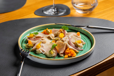 Elegant angerichtetes Gericht auf einem grünen Teller, serviert auf einem gedeckten Restauranttisch mit Besteck, Weinglas und Wasserglas im Hintergrund.